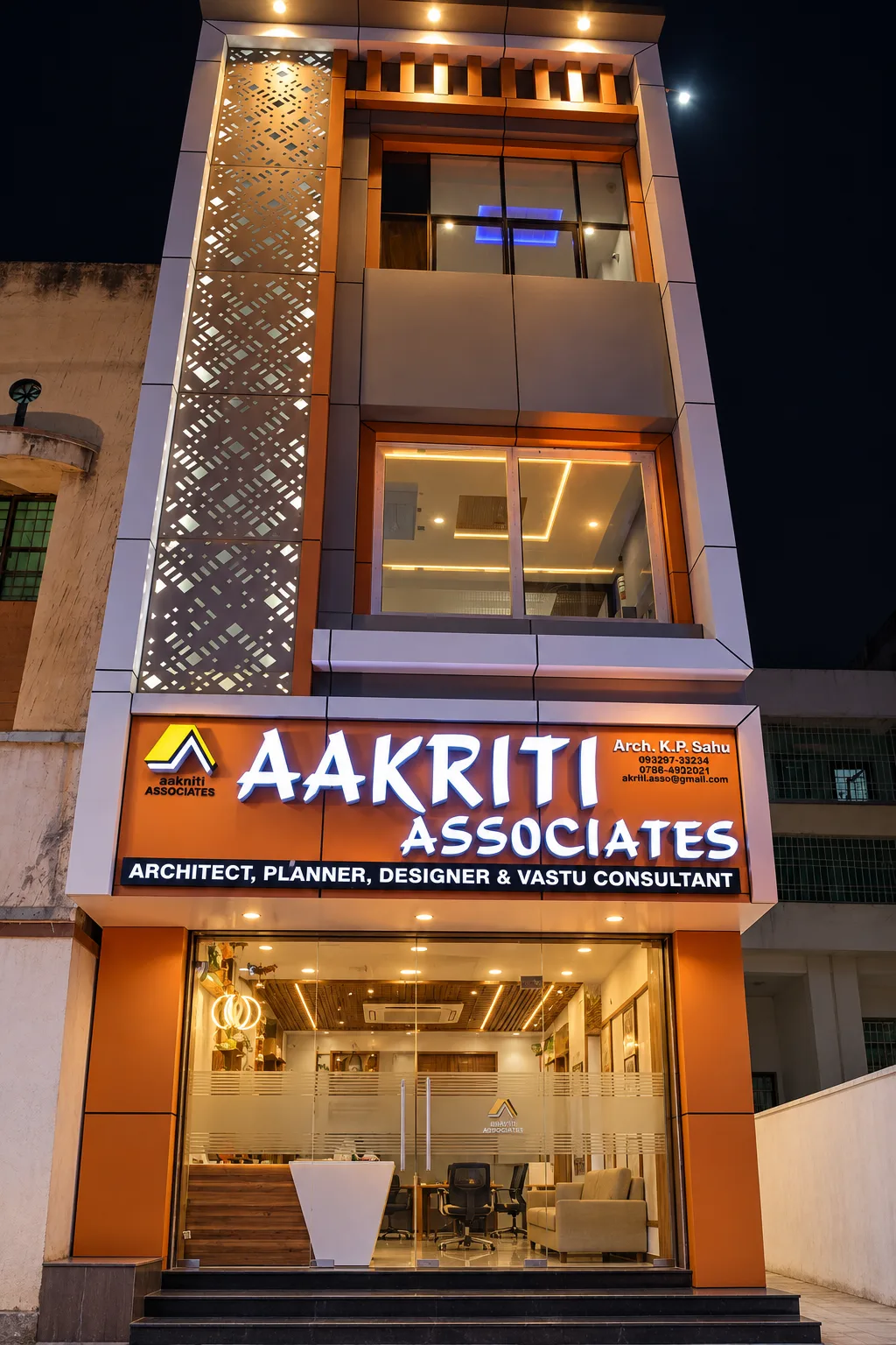 The Aakriti Associates building at night, its perforated screen and signboard lit